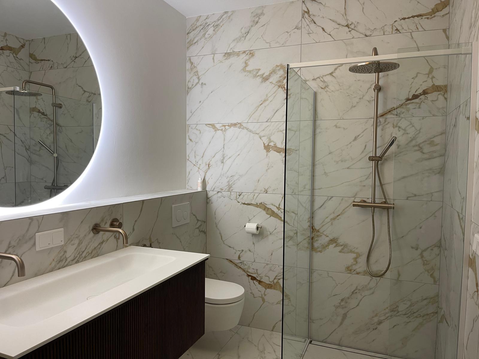 Luxe badkamer met marmer tegelwerk en ronde LED spiegel